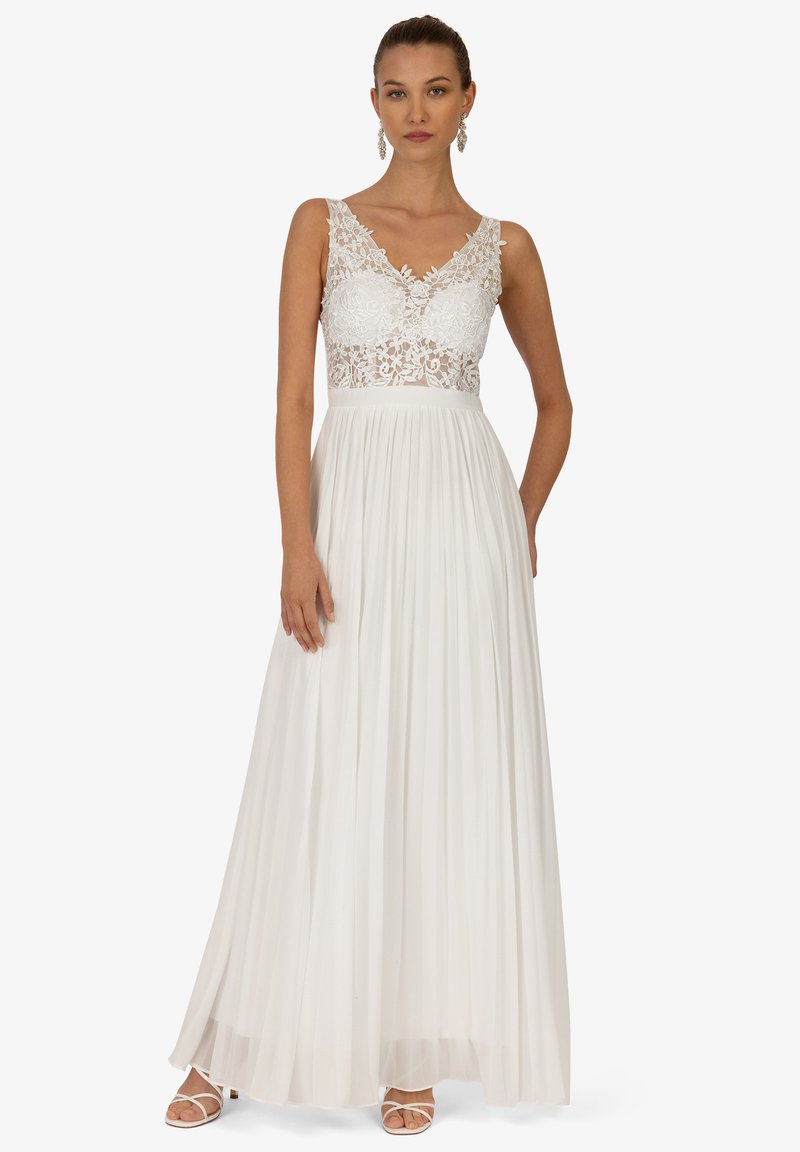 Weißes Kleid mit Spitzentop, V-Ausschnitt und plissiertem Rock. Das bodenlange Design weist aufwendige Blumenmuster und durchscheinenden Stoff auf.