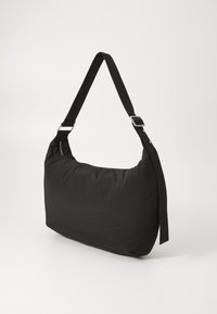Bolsa de hombro de nailon negra con cierre de cremallera, amplia correa y un diseño suave y esponjoso. Presenta herrajes en tono plateado y una silueta minimalista.