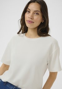 Vit kortärmad t-shirt med rund halsringning, tillverkad av mjukt tyg. Har en avslappnad passform och slät textur, bärs med blå jeans.