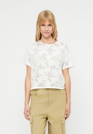 Top corto de encaje blanco con patrón floral y mangas cortas. Textura suave, escote redondo y dobladillo recto. Combinado con pantalones cargo beige.