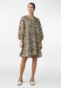 Robe florale marron avec des motifs blancs, décolleté en V, manches bouffantes et silhouette évasée, assortie à des chaussures à talons bloc crème.