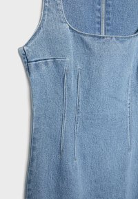 Jasnoniebieska sukienka bez rękawów z denimu z widocznymi przeszyciami i częściowo widocznym zamkiem błyskawicznym z przodu na białym tle.