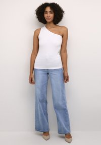 Top sin mangas de canalé blanca con un hombro, combinado con jeans anchos de talle claro y tacones de punta beige. Textura suave, diseño minimalista.