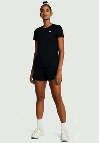 Conjunto de t-shirt e calções atléticos pretos. A t-shirt tem decote redondo e logótipo; os calções são justos. Modelo calça ténis brancos com meias.