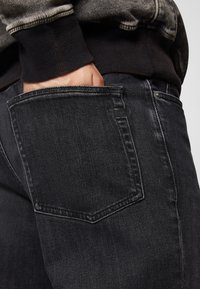 Zwarte denim jeans met een rechte pijp, zichtbare achterzak met een lichte vervaging en een gestikte rand langs de zak.