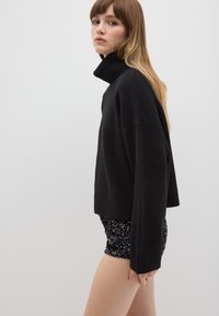 Schwarzer, gerippter Rollkragenpullover mit lockerer Passform. Hergestellt aus weichem Material, mit langen Ärmeln und cropped Länge. Glänzende Pailletten-Shorts.