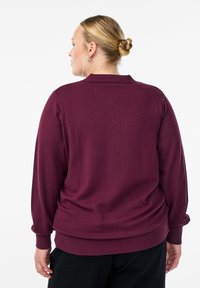 Suéter de punto burdeos con cuello de camisa, puños acanalados y dobladillo. Textura suave con un ajuste holgado, diseñado para la comodidad.