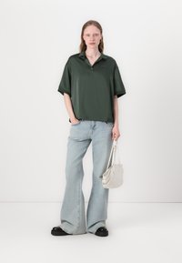 Mørkegrønn, kortermet polo skjorte med krage, kombinert med lyseblå, flagrende jeans. Modellen holder en hvit, strukturet håndveske.