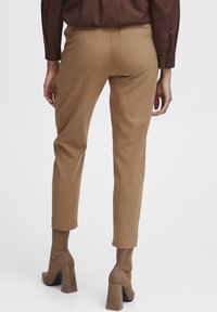 Braune, taillierte Hosen mit schlankem Schnitt, ausgestattet mit glatter Textur, seitlichen Taschen und passenden, taillierten Ankle Boots mit dickem Absatz.