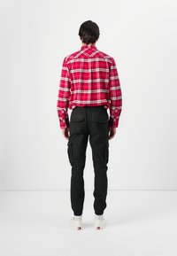 Camisa de franela a cuadros en rojo y negro, de manga larga y con cuello, combinada con pantalones cargo negros con bolsillos laterales, y calzada con zapatillas blancas.