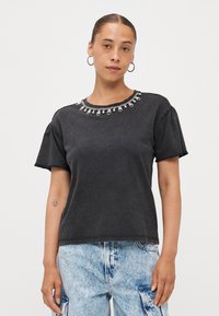 Zwarte katoenen t-shirt met korte mouwen en een ronde halslijn, versierd met heldere en zilveren versieringen langs de kraag.