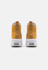 Zapatillas de lona altas amarillas con suelas de goma blancas, que cuentan con un lazo en la parte trasera, parche con el logo de Converse y detalles de costura texturizada.