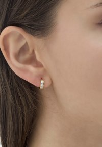 Zelta auskaru gredzens ar trim maziem caurspīdīgiem akmeņiem, ar pulētu apdari un gludu, noapaļotu dizainu. Valkāts uz auss.