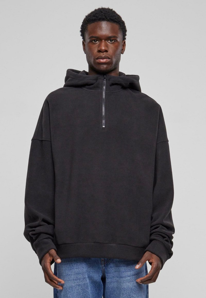 Sort zip-up hoodie lavet af blød stof, med en stor hætte, løs pasform og ribbede manchetter. Kombineret med blå denim jeans.