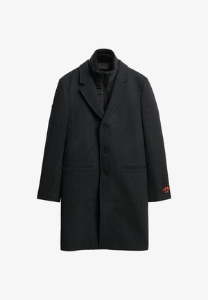 Donkergrijze wollen overjas met een geknipte revers, drie knopen, twee voorzakken en een verborgen zwarte gewatteerde voering. Rode logodetail op de mouw.