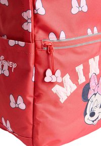 Röd ryggsäck med en stor design av Minnie Mouse, rosa rosett-mönster, broderad text och en rosa dragkedja med en rosett som accent.