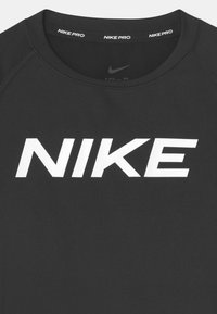 Czarna koszulka sportowa Nike Pro z białym napisem "NIKE" na wysokości klatki piersiowej i powtarzającym się napisem "NIKE PRO" wewnątrz kołnierza.