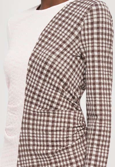 Tricou cu mânecă lungă, cu un material texturat de culoare roz deschis pe o parte și un model în carouri maro și alb pe cealaltă parte, cu detalii pliate.