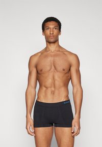 Schwarze Boxerbriefs mit leichtem Glanz, aus einem weichen Material gefertigt. Verfügt über einen breiten Bund mit blauem "SLOGGI"-Logo.