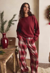 Viininpunainen collegepaita yhdistettynä punaisiin ja ruudullisiin pyjamahousuihin, joissa on valkoiset ja laivastonsiniset yksityiskohdat. Mukava rakenne, rento istuvuus.