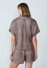 Conjunto de pijama de piel de leopardo que incluye una camiseta de manga corta y pantalones cortos a juego, confeccionado en una tela suave y lisa, con tonos rosas y negros.