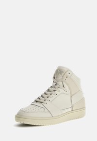 Sneaker alte in pelle beige chiaro, caratterizzate da perforazioni, cuciture tonali e una collare imbottito per il supporto. Lacci piatti e suola in gomma.