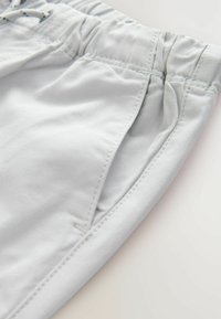 Shorts gris clair avec une ceinture élastique, doté de poches latérales et d'un tissu lisse et texturé. Détail de cordon de serrage inclus.