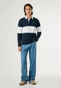 Marineblå og hvit stripete langermet polo med krage, kombinert med lyseblå jeans og brune slip-on sko. Enkel, avslappet design.