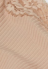 Nude stof met een geribde structuur, voorzien van delicate kantafwerking langs de bovenrand. Het materiaal is zacht en rekbaar.