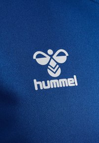 Kék szövet, amelyen egy fehér méhecske logó található, alatta a "hummel" felirattal. A textúra simának tűnik, és puha, sportos anyagból készült.