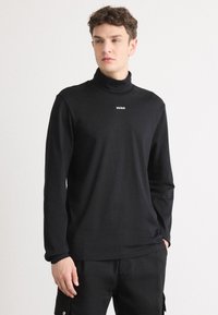 Svart langermet høyhalset genser laget av myk stoff, med en liten hvit "HUGO" logo på brystet. Enkel, tettsittende design med minimal detaljer.