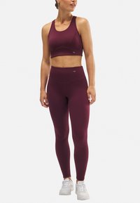 Conjunto de sujetador deportivo y leggings en burdeos, fabricado con una tela elástica y texturizada. Presenta un diseño ajustado, tirantes anchos y cintura alta.