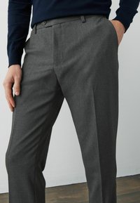 Pantalones gris claro de corte a medida con una textura suave, diseño de pierna recta, parte frontal plana y cierre de botón, combinados con un suéter azul marino.