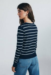 Světle modré džíny s navy pruhovaným svetrem bílými horizontálními pruhy, žebrovanými manžetami a pasem. Pohled zezadu, ukazující design a střih.