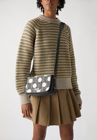 Borsa a tracolla con una cintura in pelle nera, tessuto testurizzato bianco e nero con grandi pois e una forma rettangolare strutturata.