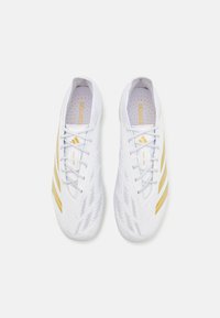 Zapatillas deportivas blancas con acentos dorados, que cuentan con un upper texturizado, cordones planos y tres rayas distintivas a cada lado.