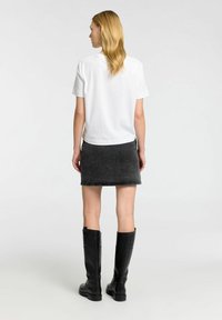 Bílá trička s krátkým rukávem v kombinaci s tmavě šedou denimu mini sukní a černými kozačkami po kolena. Hladká textura a ležérní design.