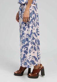 Robe maxi en tissu rose clair avec des imprimés floraux et animaliers bleus. Associée à des sandales à plateforme marron avec une semelle épaisse noire.