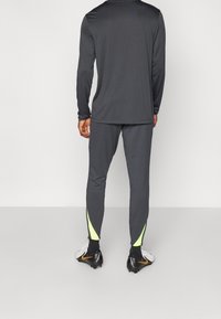 Atletische kleding met een lange, donkergrijze top en bijpassende slim-fit broek met neongele accenten en ritsen bij de enkels.