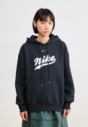 Svart Nike hettegenser med en stor hvit logo, med en frontlomme og snorer. Stoffet ser mykt ut med en avslappet passform.