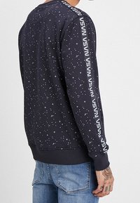 Felpa blu con stampa stellata, polsini a costine e dettaglio del logo verticale lungo la manica sinistra. Tessuto morbido in misto cotone.