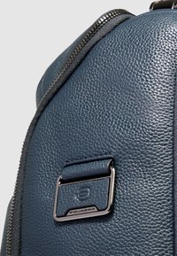 Mochila de cuero azul marino con superficie texturizada, detalles de herrajes plateados y una cremallera visible a lo largo del lateral.