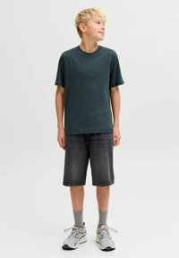 Camiseta de algodón verde oscuro con texto en relieve "ORIGINALS", combinada con pantalones cortos de mezclilla gris. Zapatillas gris claro y calcetines de canalé completan el conjunto.