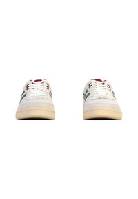 Een paar witte sneakers met beige zolen, rode accenten bij het vetersysteem en groene zijstrepen, weergegeven vanaf de voorkant op een witte achtergrond.