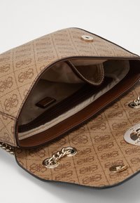 Brun mønstret håndtaske med guldkæde og magnetisk lukning. Indersiden inkluderer en lomme med lynlås og et mærke. Glat stoffinish.