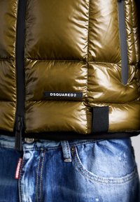 Oliven grøn pufferjakke med glat tekstur, med en sort DSQUARED2-label, frontlynlås og et sort accentbånd i kanten.