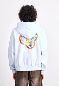 Lichtblauwe hoodie met een kleurrijk grafisch ontwerp op de achterkant met meerkleurige patronen en een gestructureerde afwerking.