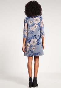 Floral print dress in light blue with three-quarter sleeves and a back button detail, featuring large pink and dark blue flowers.