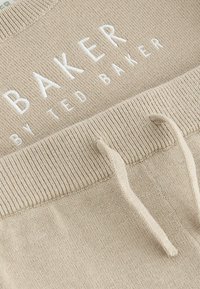 Pantalons de survêtement beige avec une taille côtelée et des cordons à nouer ; logo brodé blanc "BAKER by TED BAKER" sur le devant.