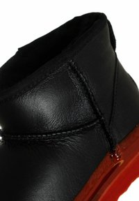 Schwarze Lederstiefelette mit glatter Oberfläche, ausgestattet mit einer genähten Naht und einer glänzenden roten Gummisohle. Kurzes Schaftdesign.